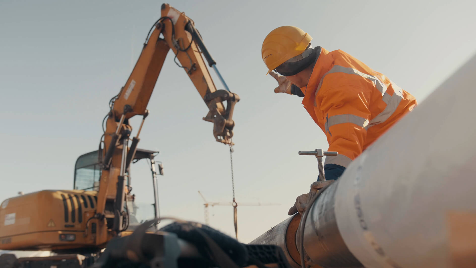 Mitarbeiter bei der Rohrverlegung neben einem Bagger auf einer Baustelle